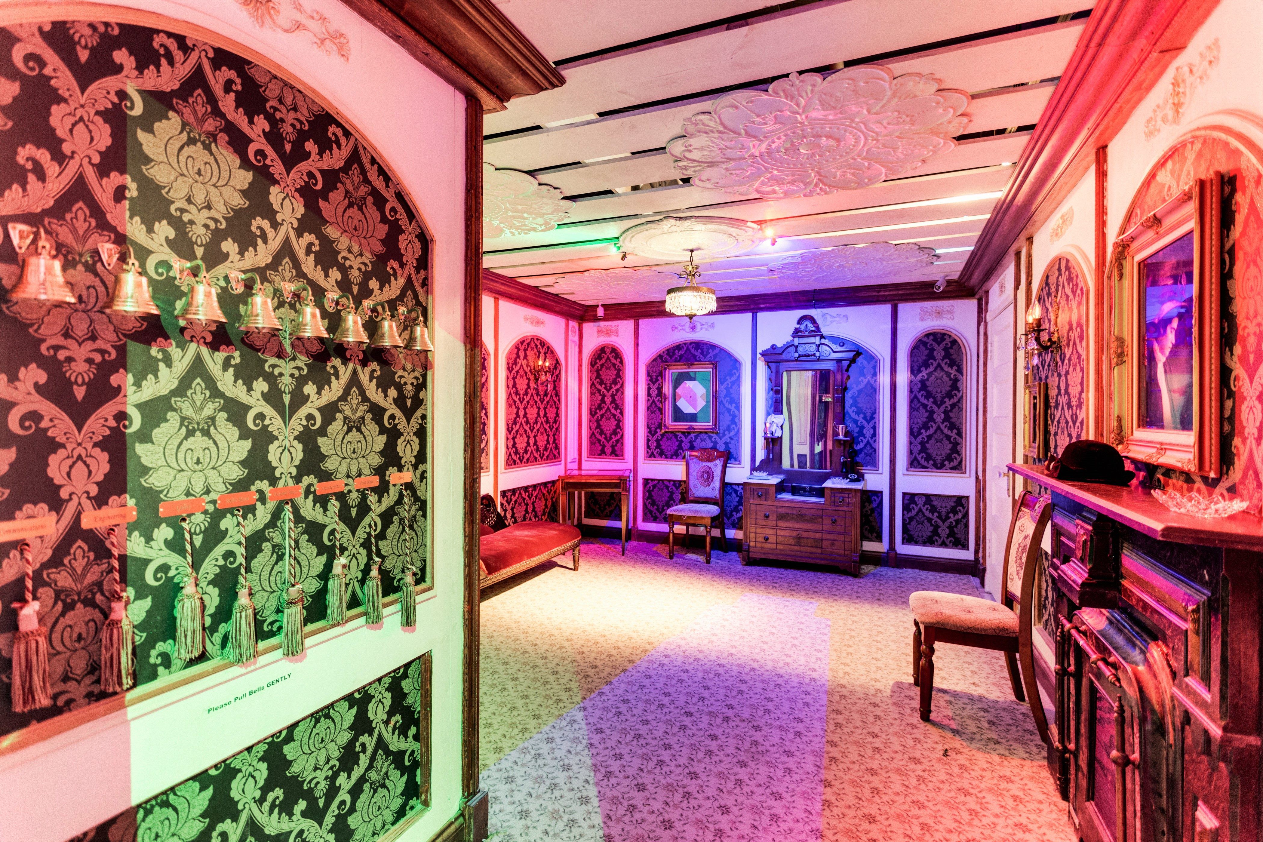 Glamorous room with patterned wallpaper, decorative bells, and colorful lighting; features a vintage mirror and seating.