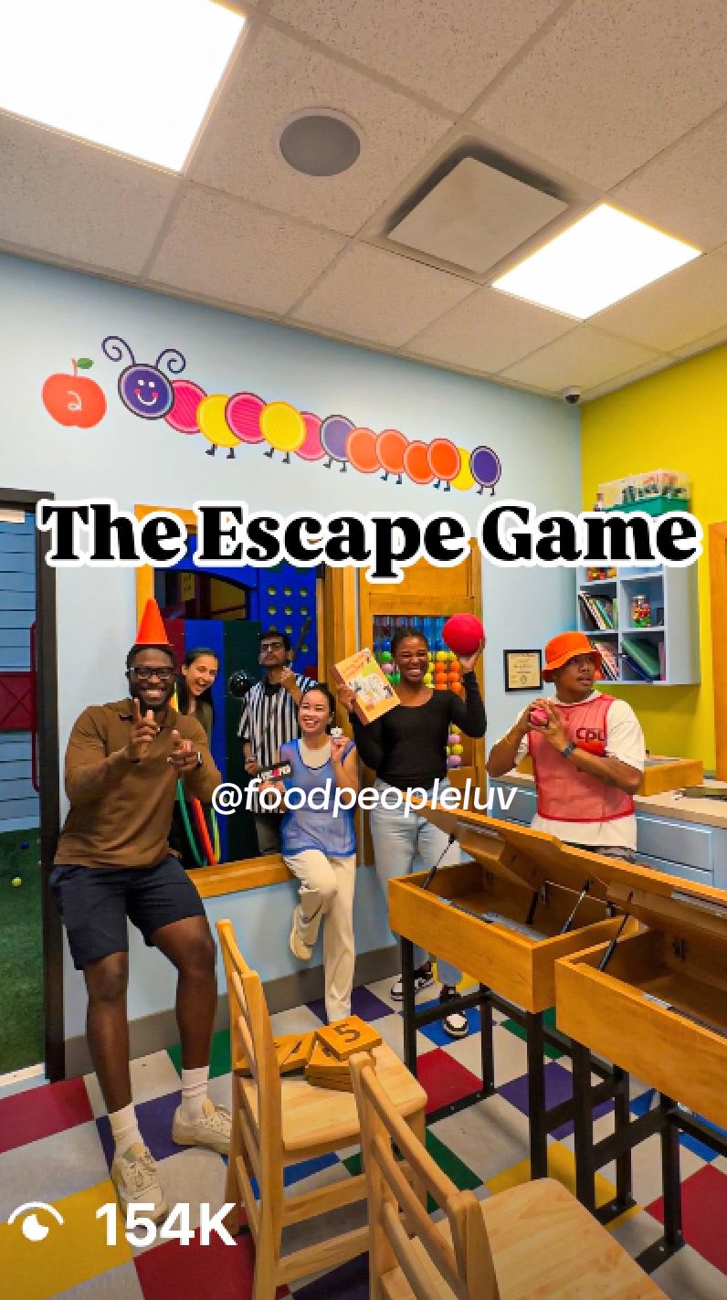 Five people pose inside a colorful room themed for an escape game. Bright decorations and game elements are visible.