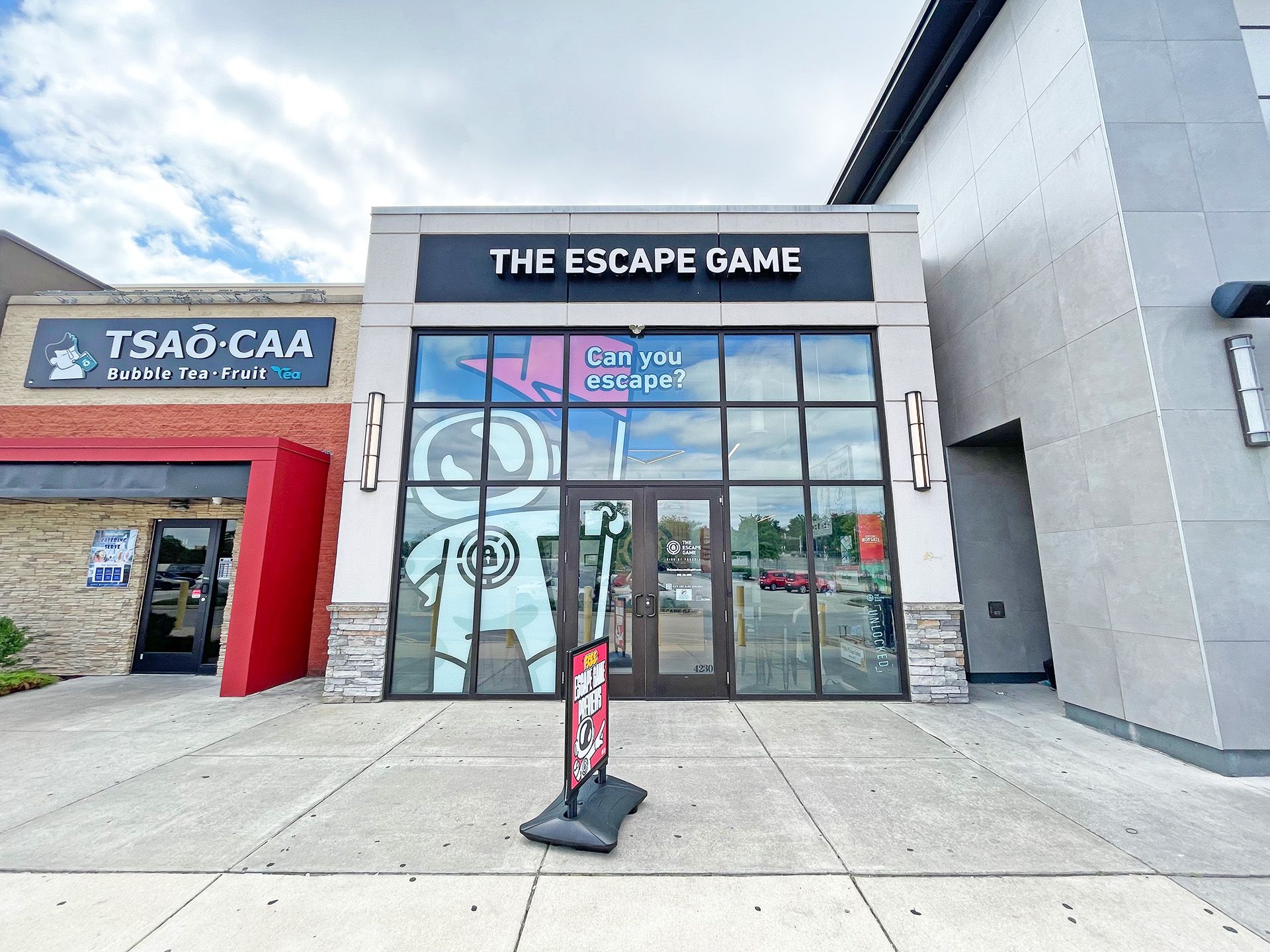 Facade of "The Escape Game" featuring large glass doors, with a sign asking, "Can you escape?" Nearby is “TSAO-CAA” for bubble tea.