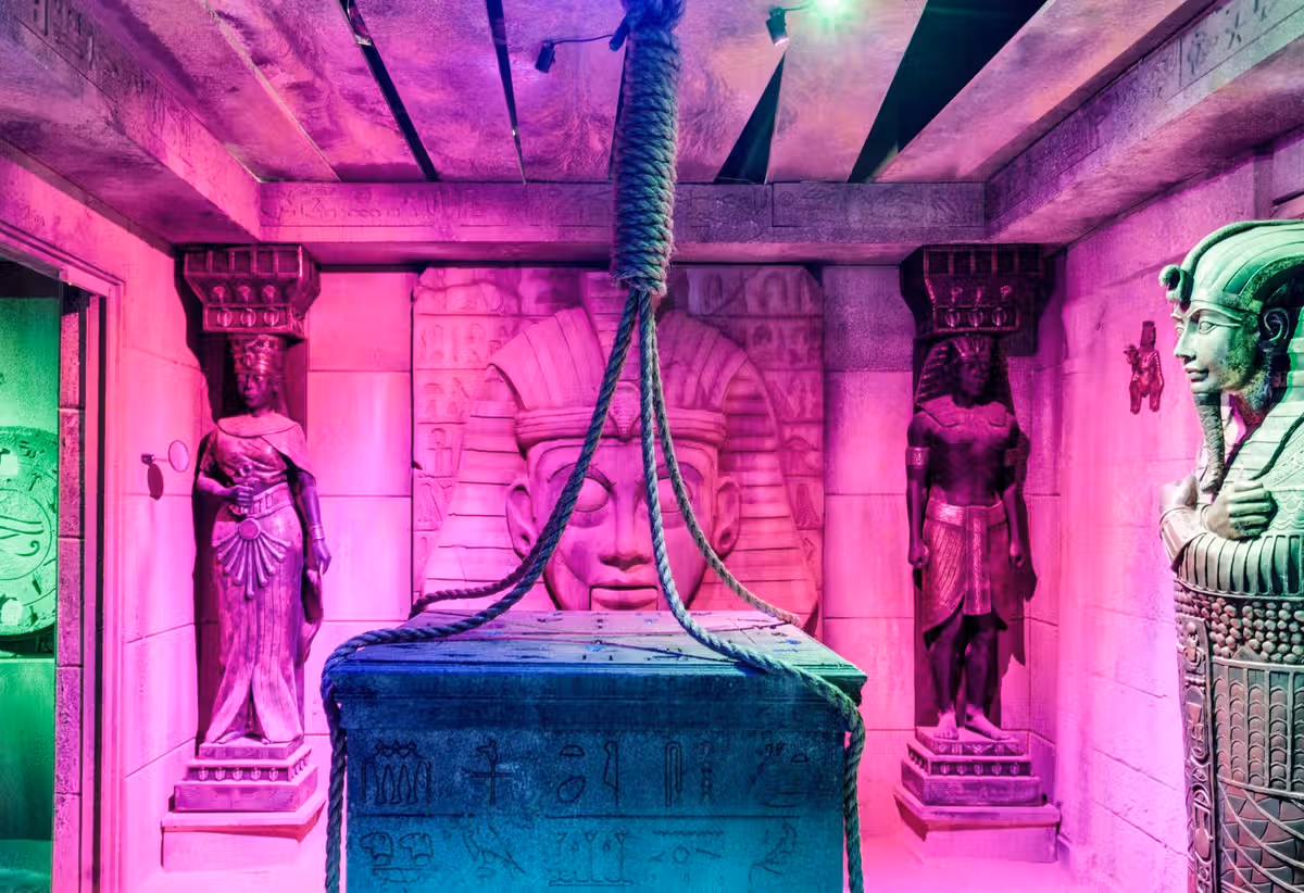 Vibrant room resembling an ancient Egyptian tomb, featuring statues, hieroglyphs, and a stone sarcophagus with a rope.