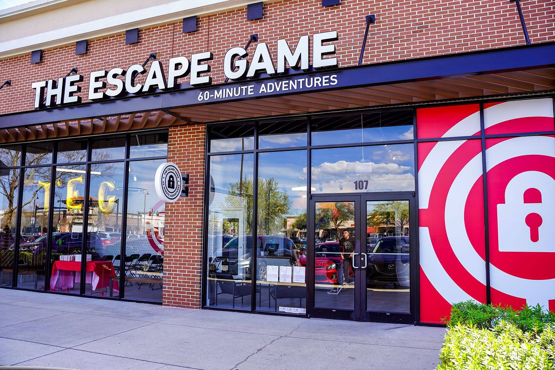 Exterior of "The Escape Game" featuring large windows, a red and white logo, and a sign for 60-minute adventures.