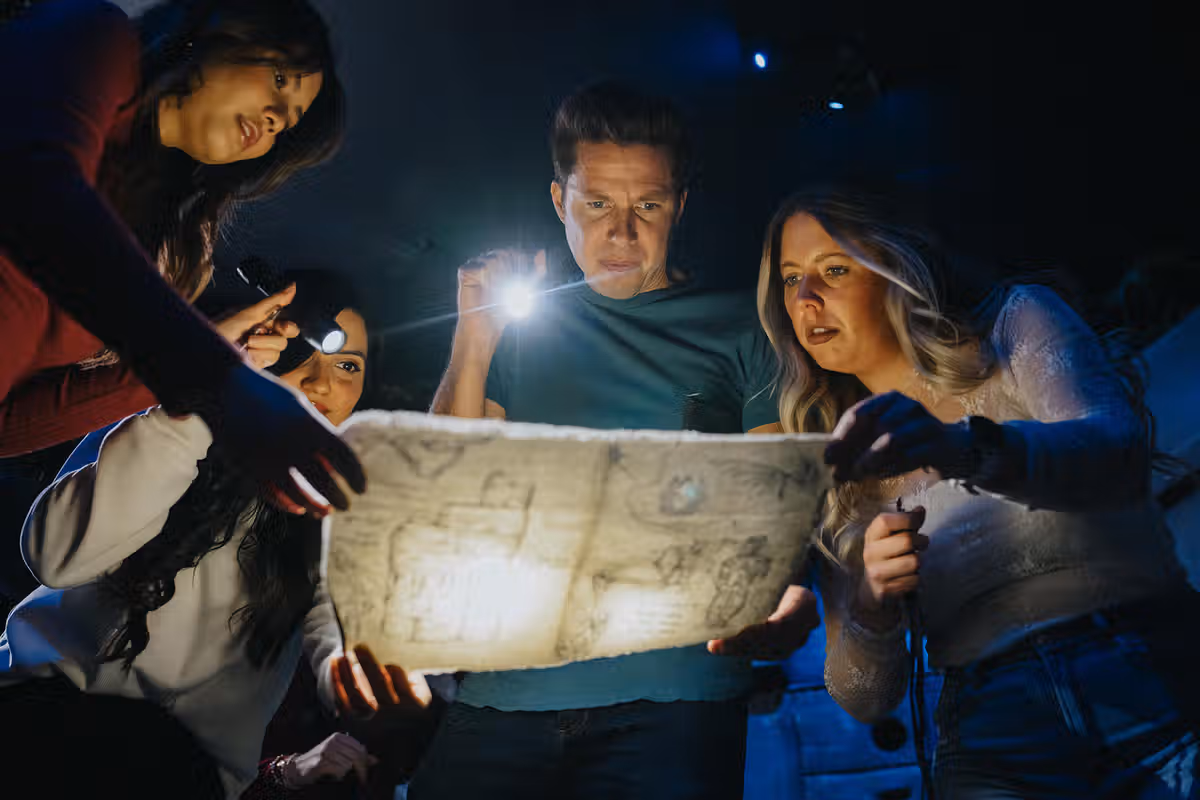 A group of four people examining a map under dim lighting, using flashlights to illuminate details.
