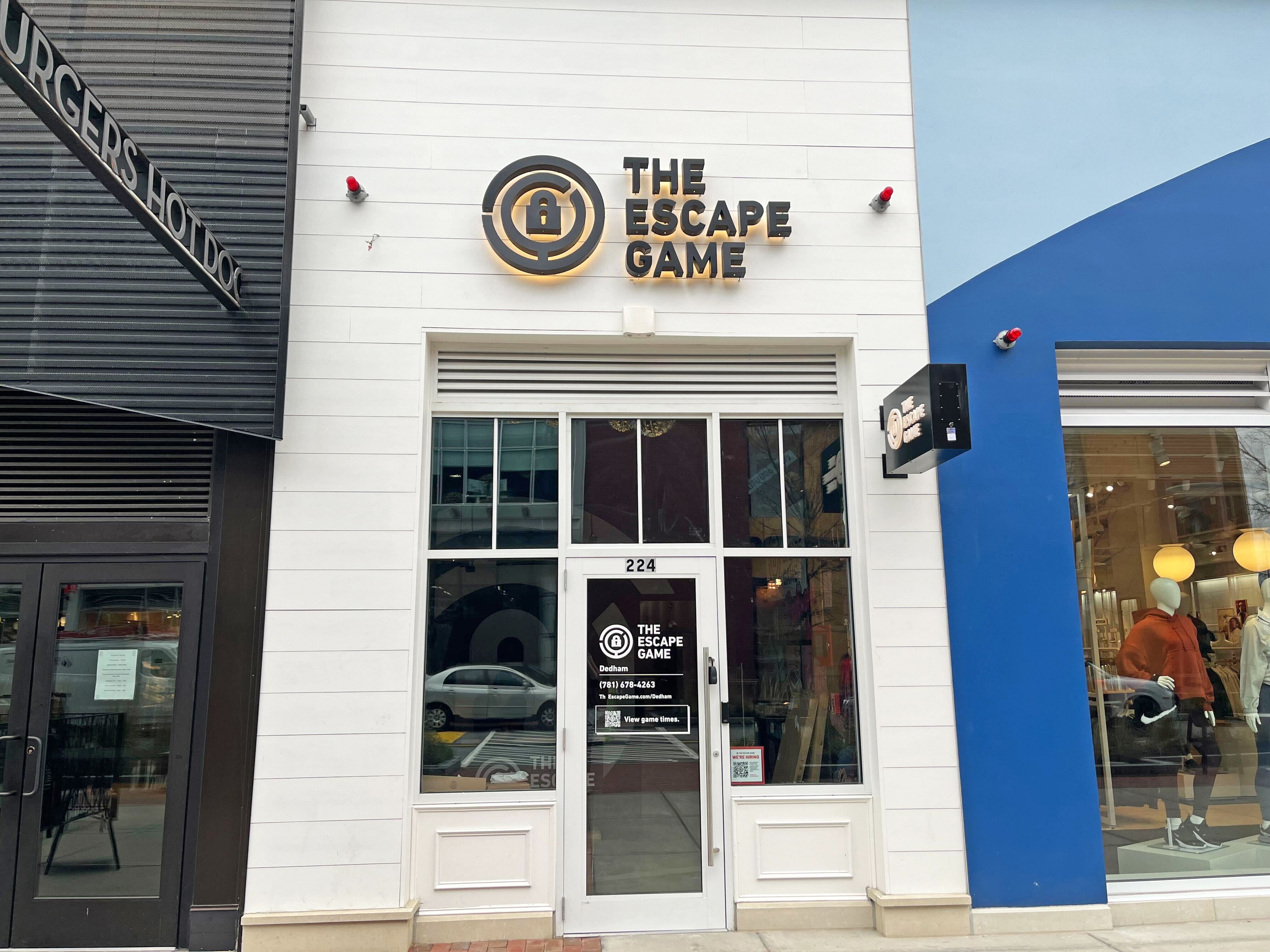 Front of "The Escape Game" with a sign above the entrance, featuring large text and a logo, neighboring a store.