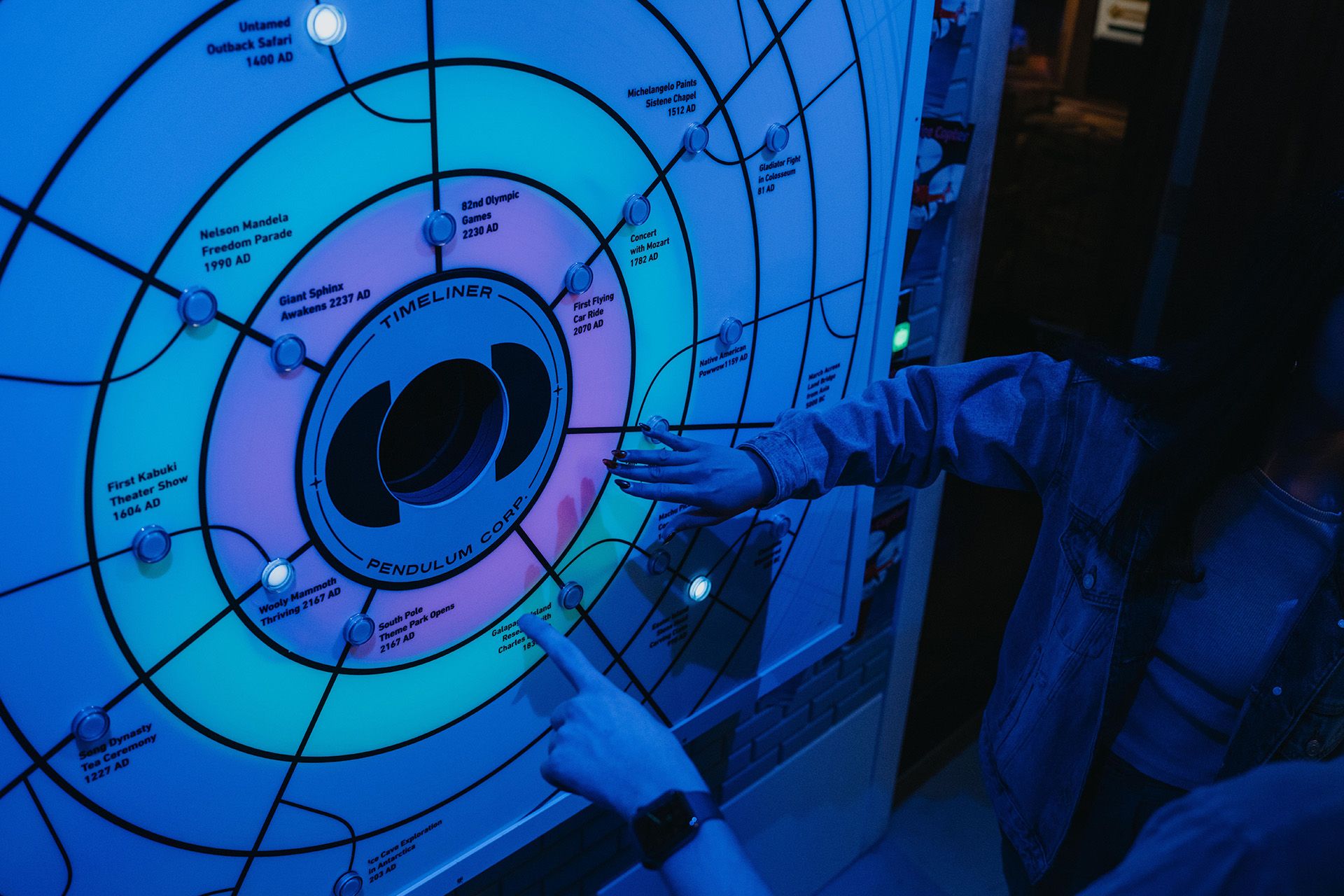A person points at a colorful timeline display with key historical events, surrounded by blue lighting.