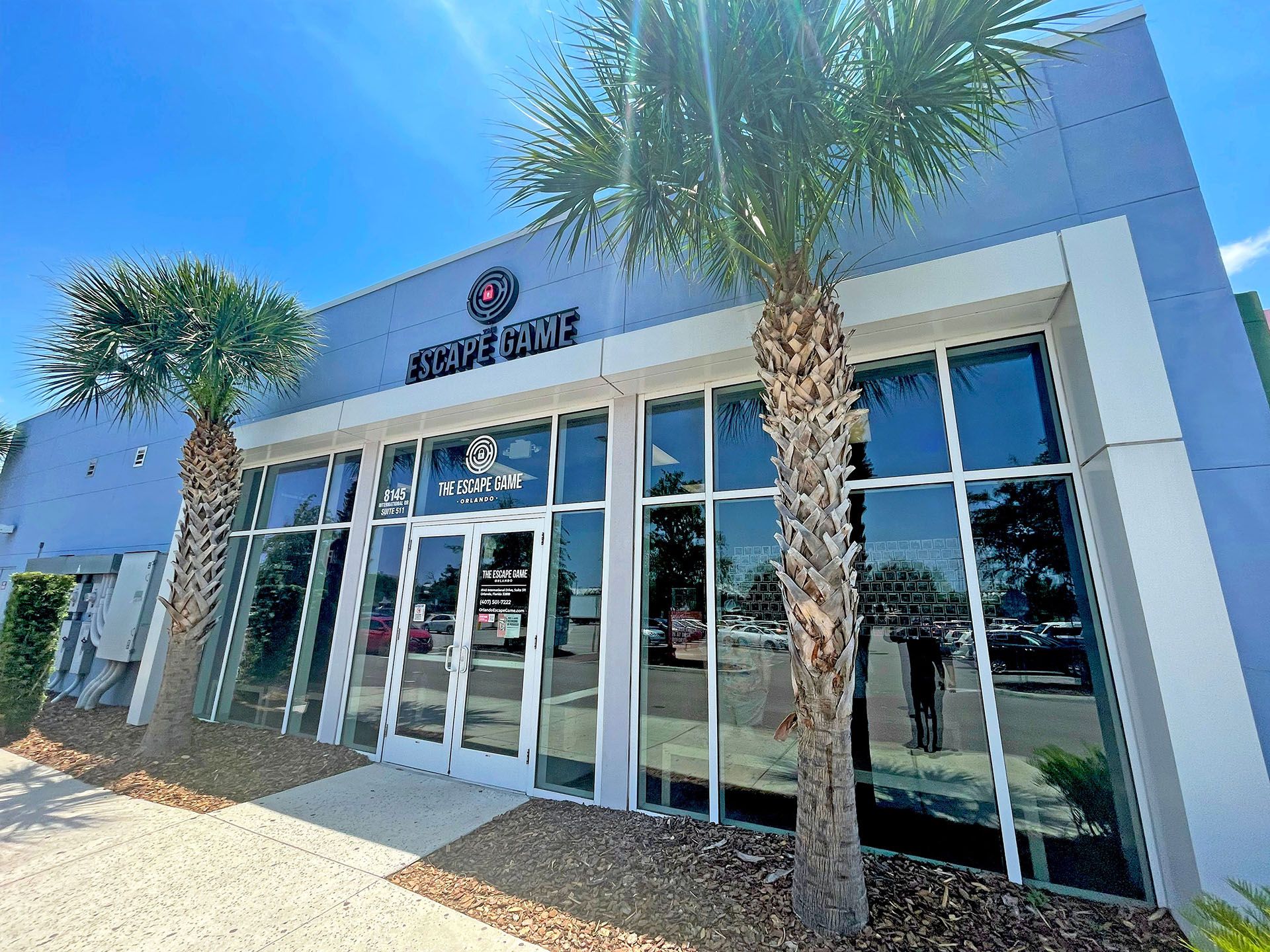 Exterior view of "The Escape Game" building, featuring large glass windows, palm trees, and a modern design.