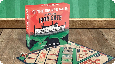 Board game box titled "Escape from Iron Gate" next to a game board with various paths and images, placed on a wooden surface.