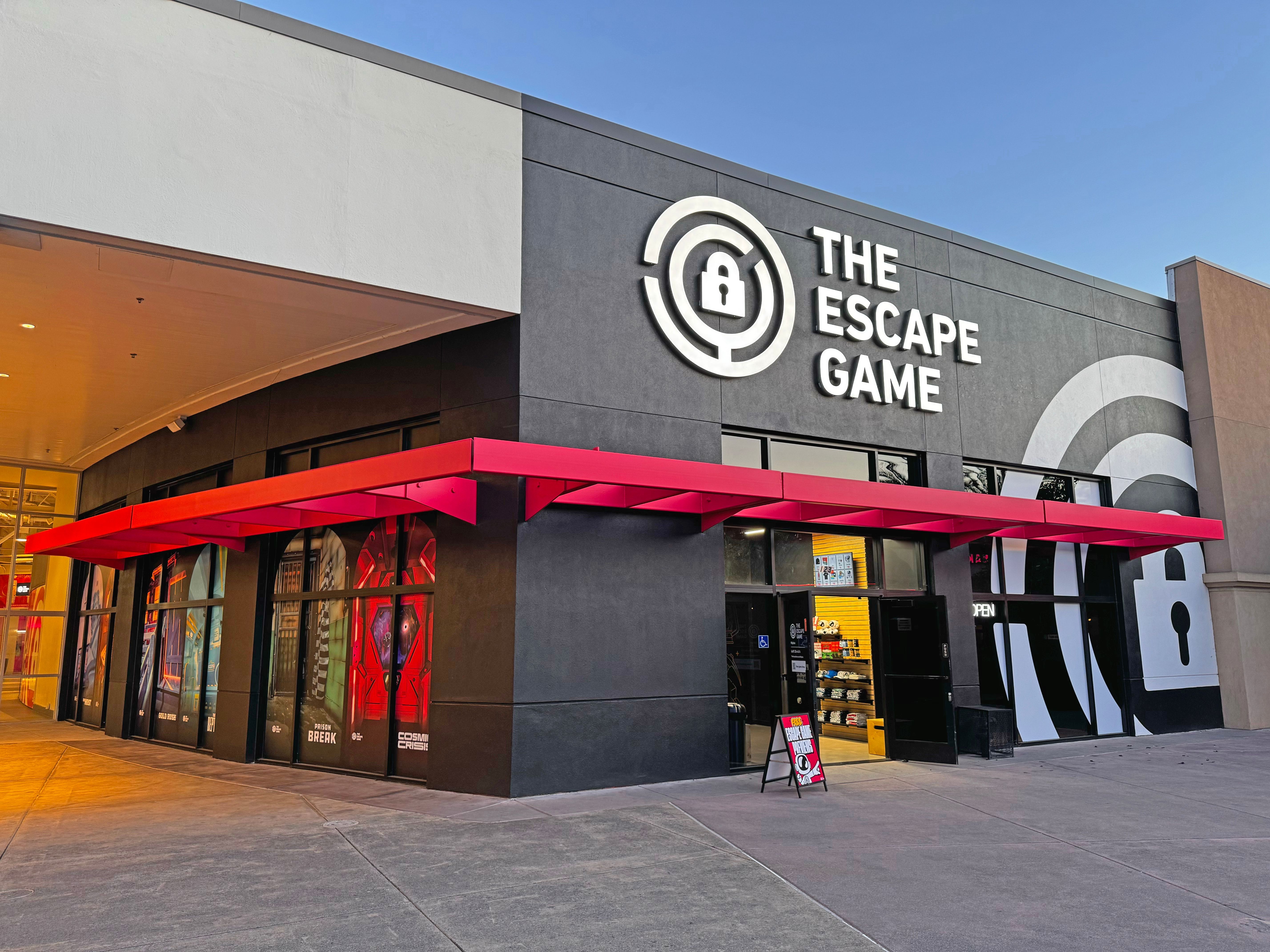 Exterior of "The Escape Game" featuring a large sign, vibrant red awning, and glass doors with game-themed windows.