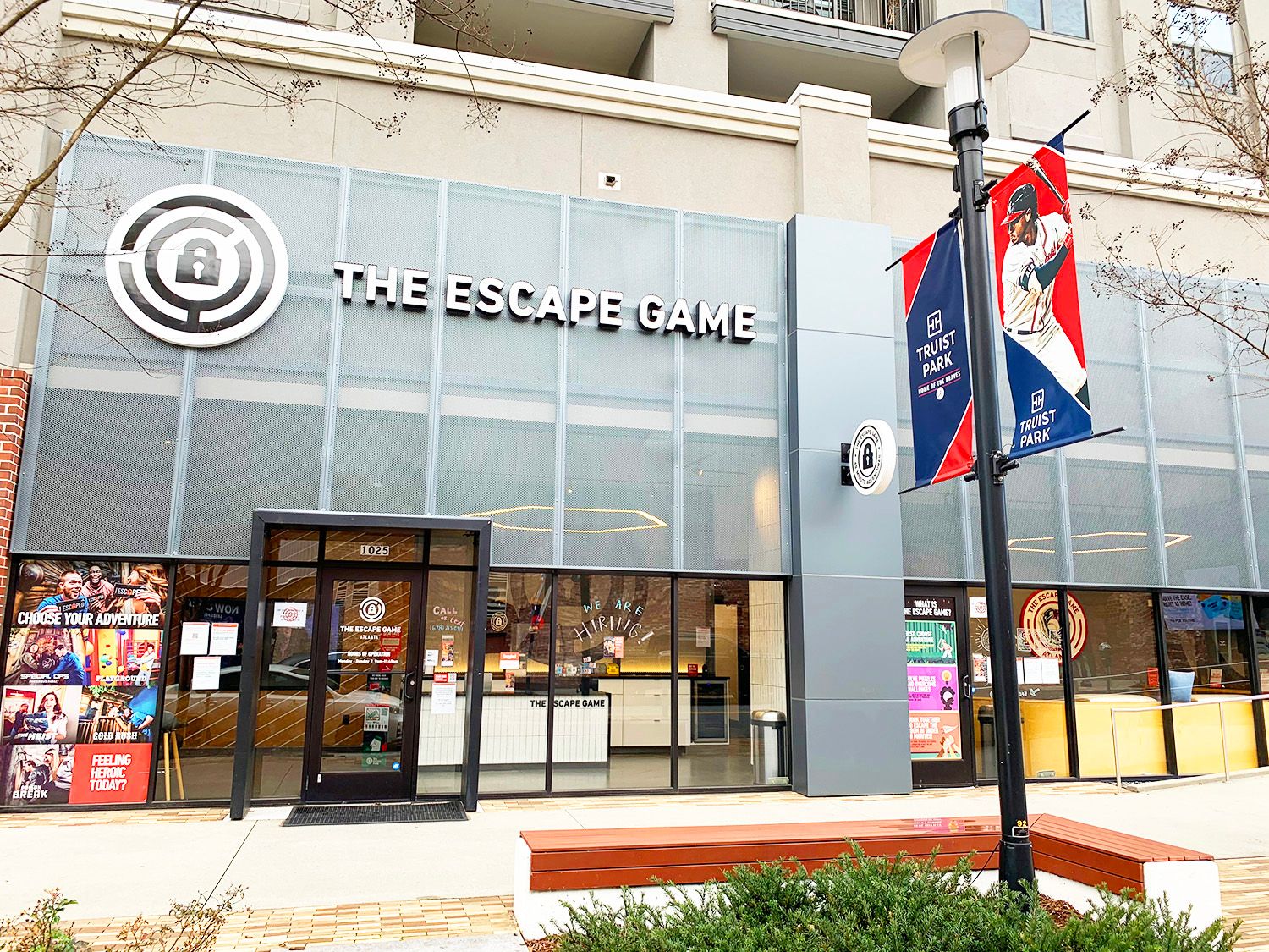 Entrance to "The Escape Game" with large signage, windows displaying promotional materials, and nearby park banners.