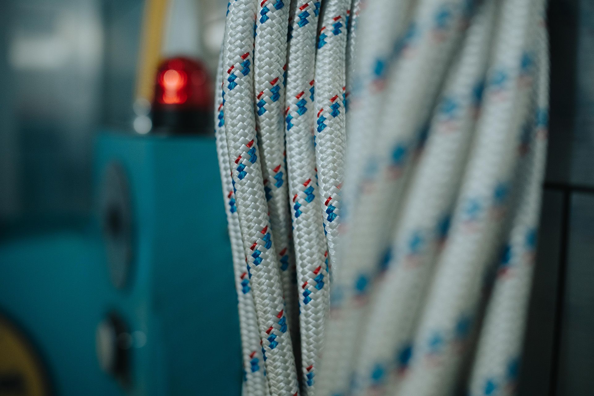Close-up of coiled white rope with red and blue patterns, next to a blue control panel with a red light.