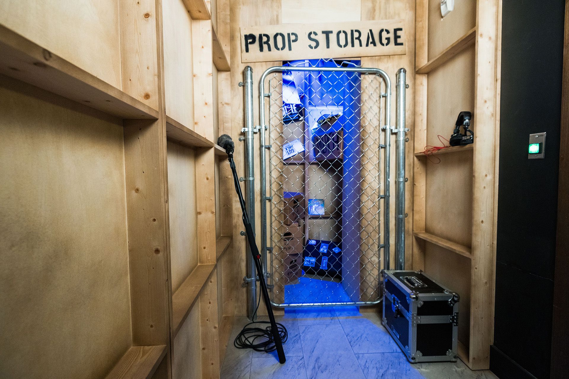 A corridor leading to a gated room labeled "PROP STORAGE," with a microphone on the floor and dim blue lighting inside.