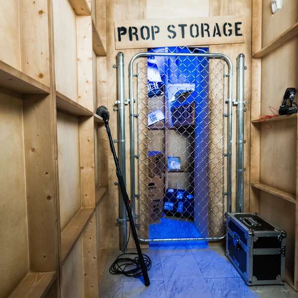 A corridor leading to a gated room labeled "PROP STORAGE," with a microphone on the floor and dim blue lighting inside.