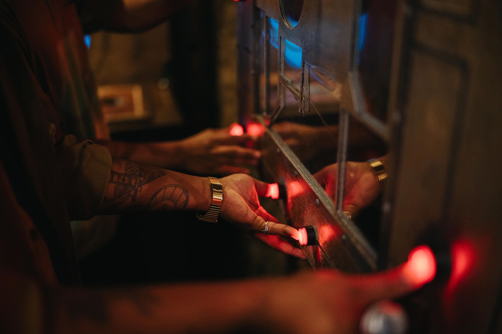 Hands pressing illuminated buttons on a control panel, with visible tattoos and a warm, dimly lit background.