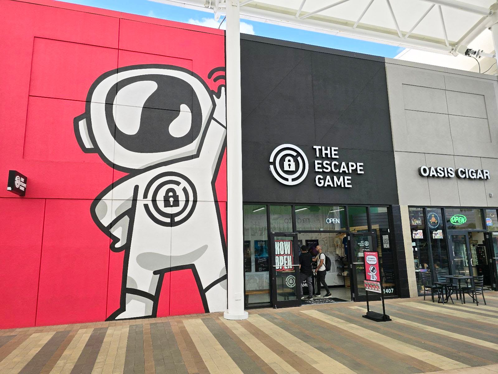Facade of a building featuring a large astronaut mural on the left and signs for "The Escape Game" and "Oasis Cigar."