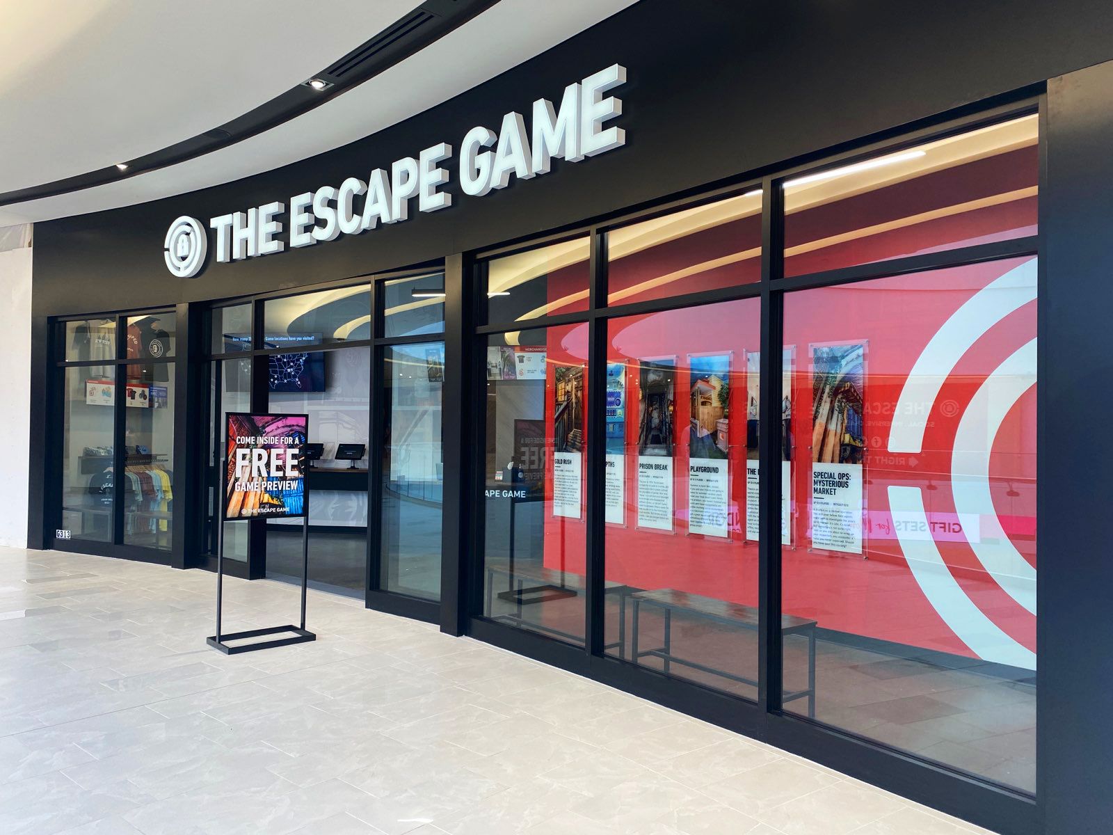 Exterior view of "The Escape Game" location, featuring glass doors, promotional signage, and game information posters.