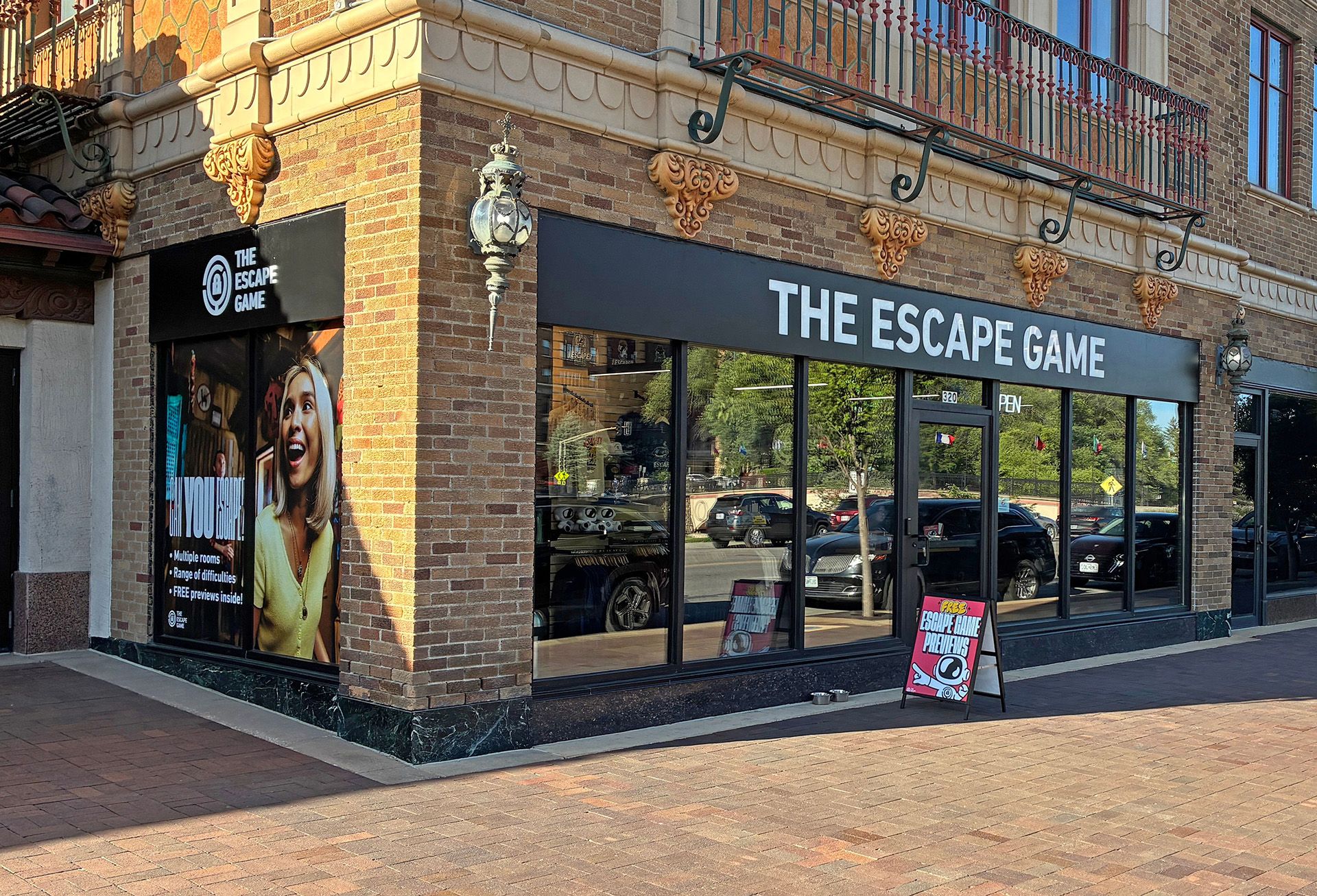 Exterior view of "The Escape Game" storefront, featuring large windows, a smiling woman on the advertisement, and a sidewalk sign.