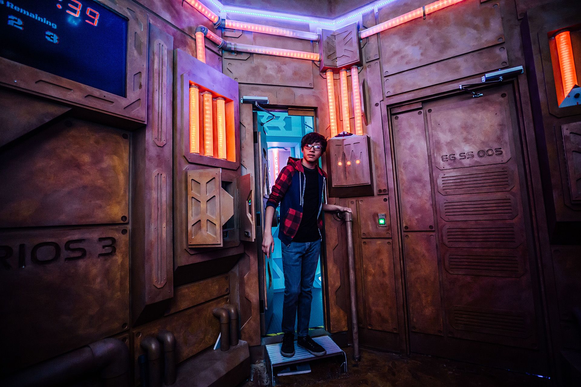 A person with glasses and a plaid shirt stands at an entrance, framed by a futuristic, illuminated room.