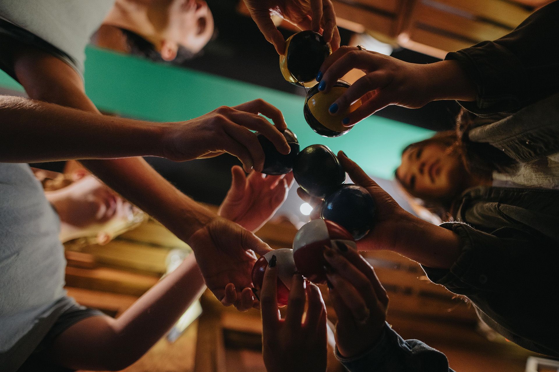 Group of hands reaching toward the center, holding colorful spherical objects, with faces partially visible in the background.