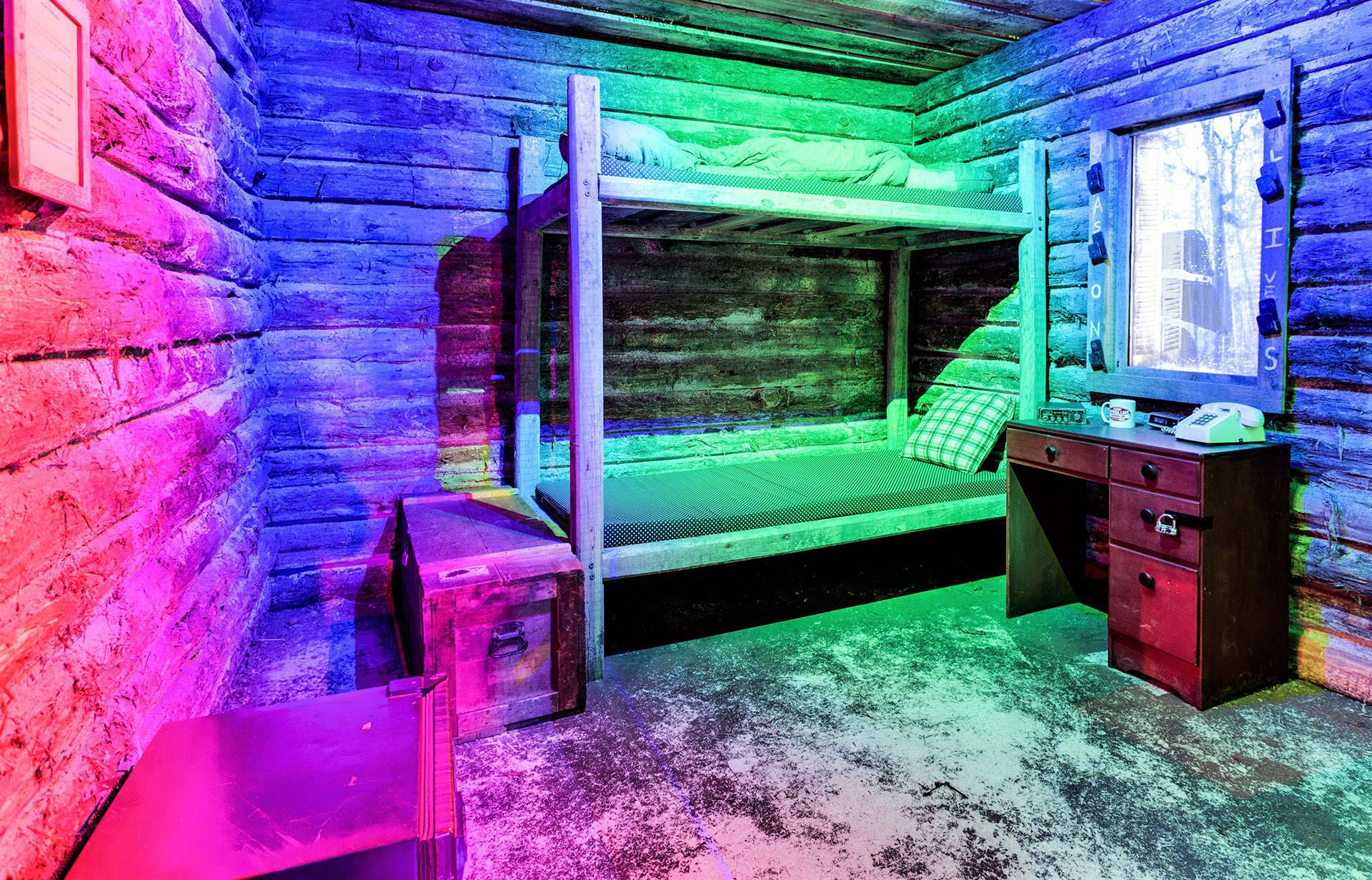 A colorful, illuminated log cabin interior features a bunk bed, a wooden desk, and vintage decor.