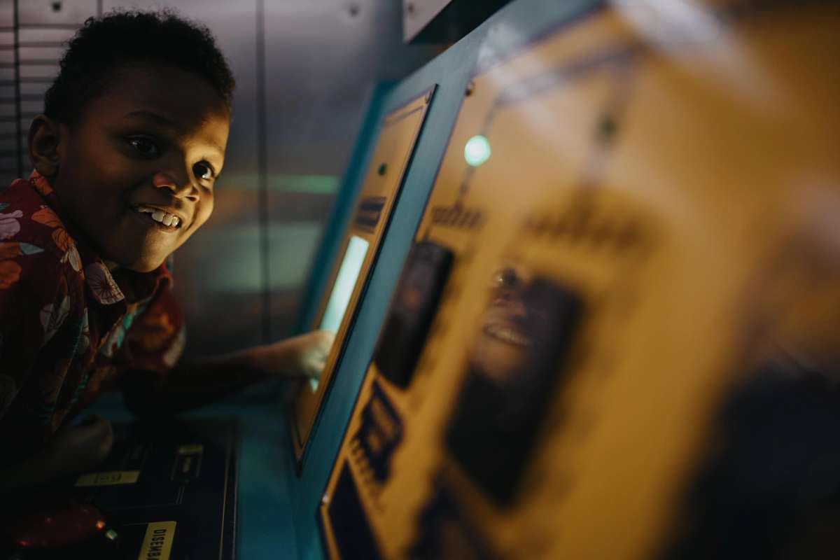 A smiling child interacts with a brightly colored control panel, focused on a glowing screen in a playful environment.