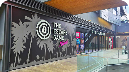 Exterior view of "The Escape Game Miami" with palm tree designs and glass entrance, showcasing colorful game promotions.