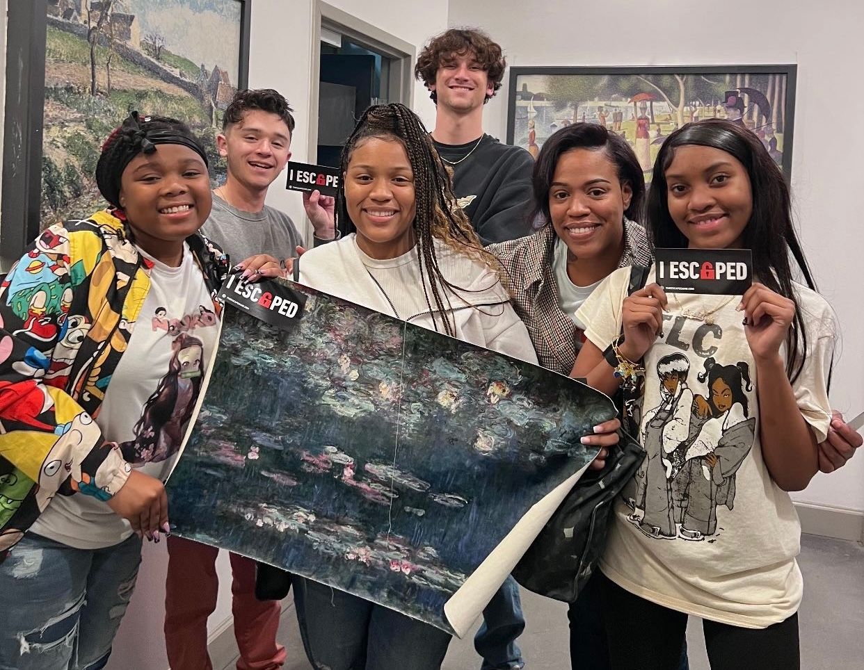 Group of six young people smiling, holding art pieces and stickers that read "I ESCAPED" in a gallery setting.