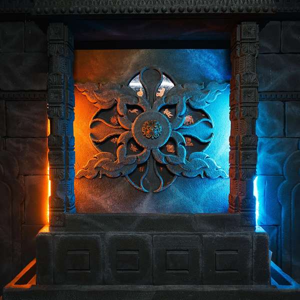 Intricately carved stone wall featuring a central floral motif, illuminated by orange and blue lights on either side.