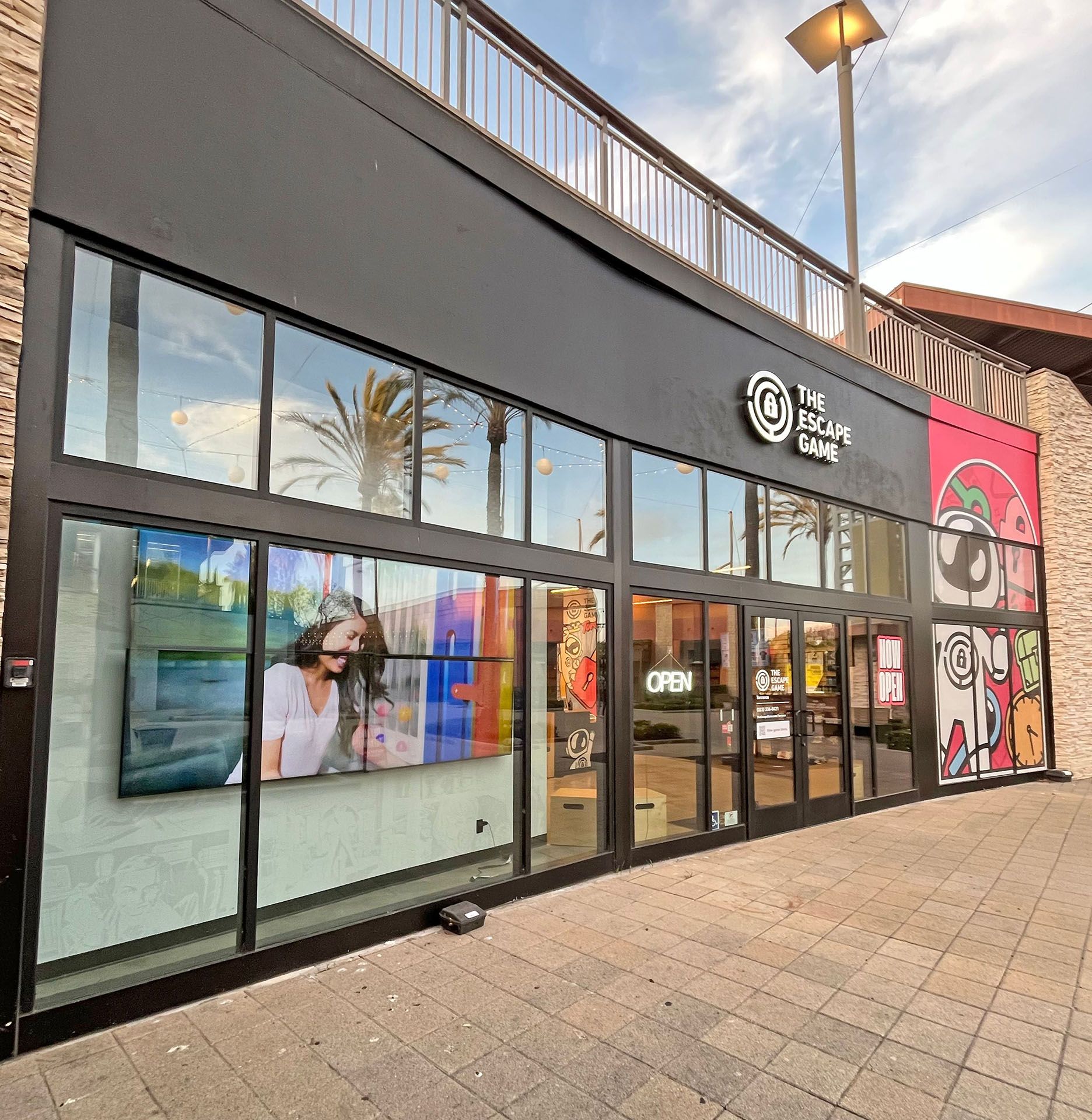 Storefront of "The Escape Game" featuring large glass windows, a digital screen, and colorful artwork on the side.