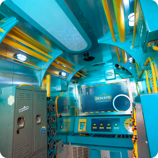 Futuristic interior of a submersible featuring teal walls, yellow pipes, control panels, and a monitor labeled "DESCEND."