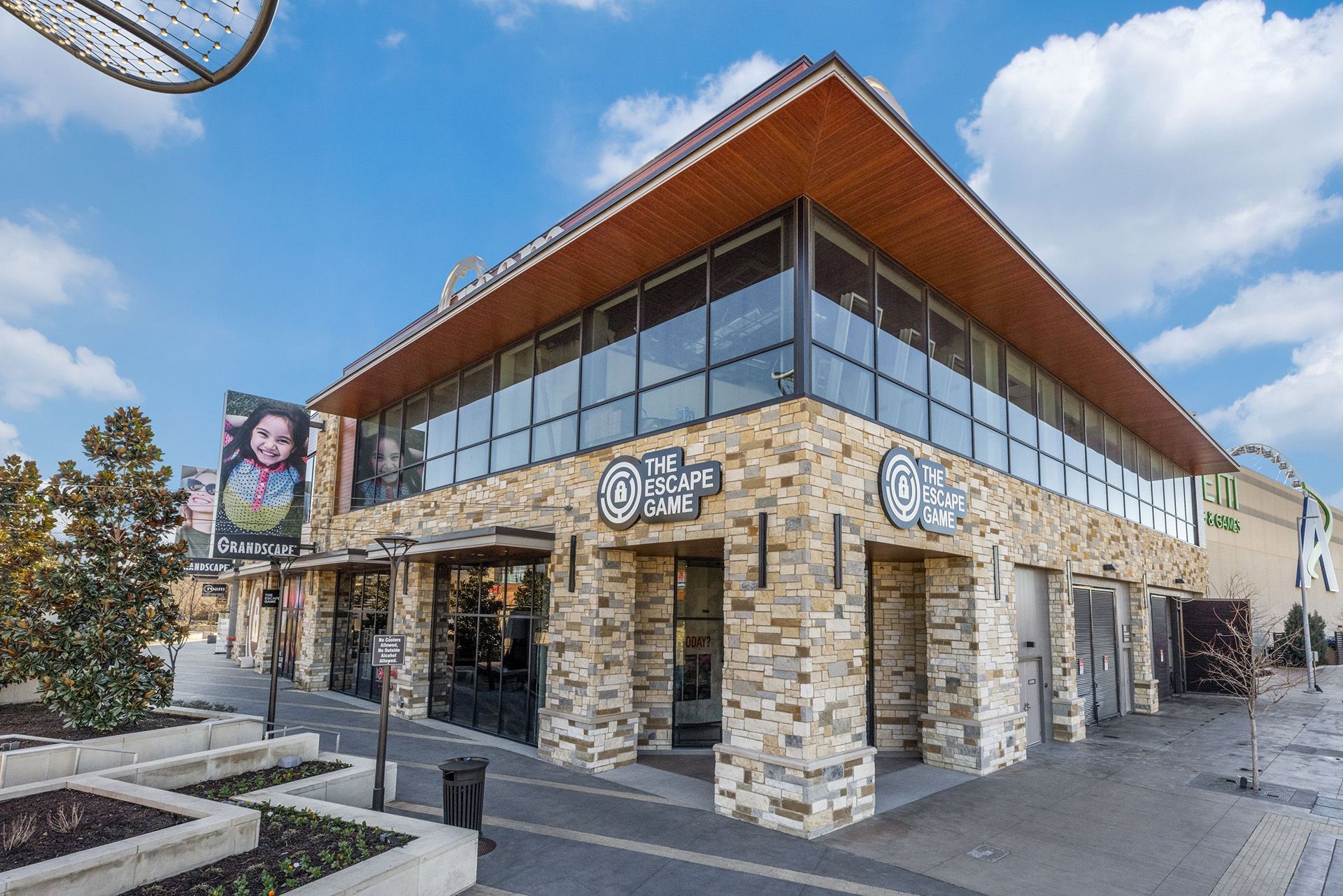 Exterior view of "The Escape Game" at Grandscape, featuring a stone facade, large glass windows, and a promotional sign.