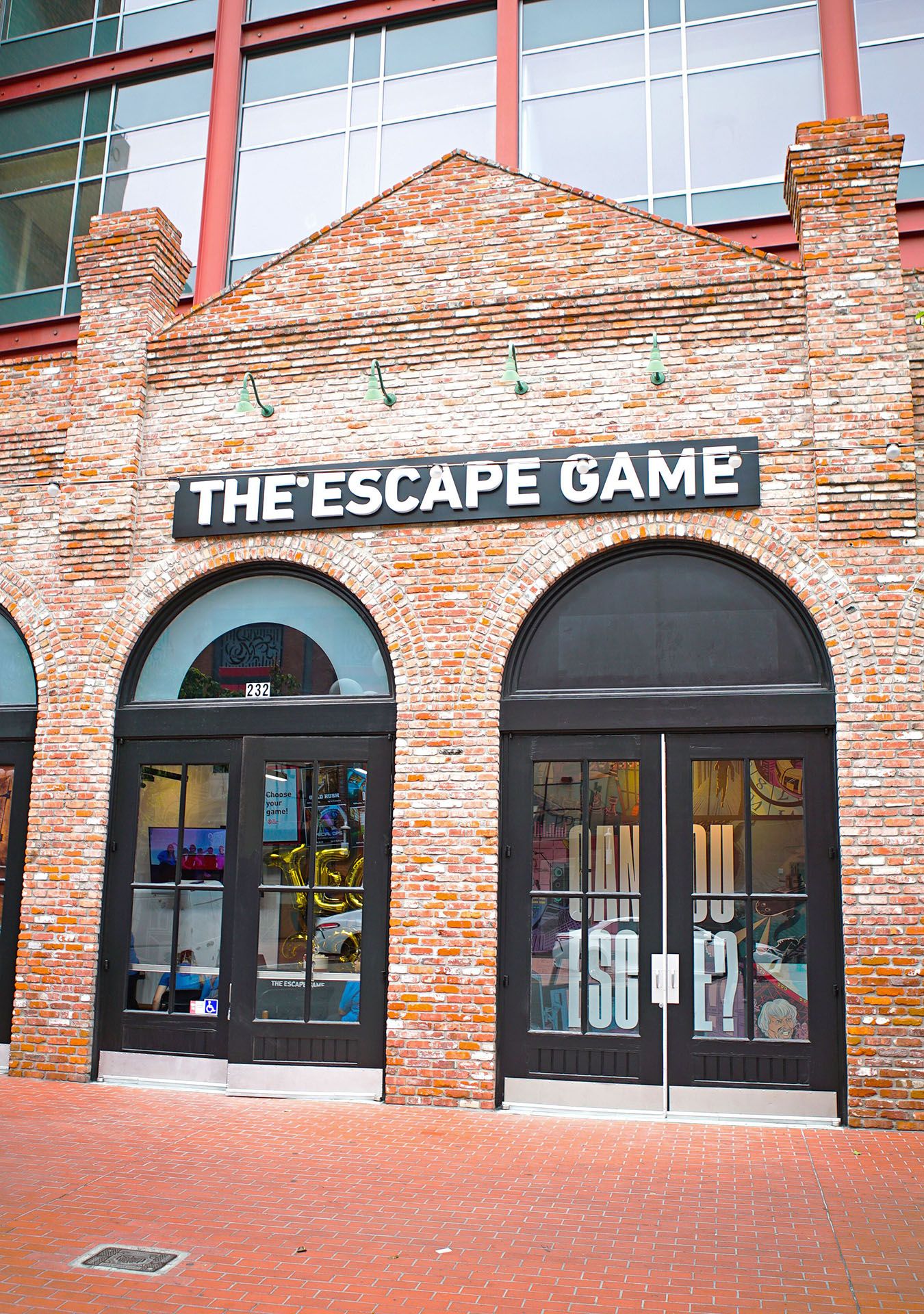 Facade of "The Escape Game" featuring a brick wall and large arched doors, with a sign above the entrance.