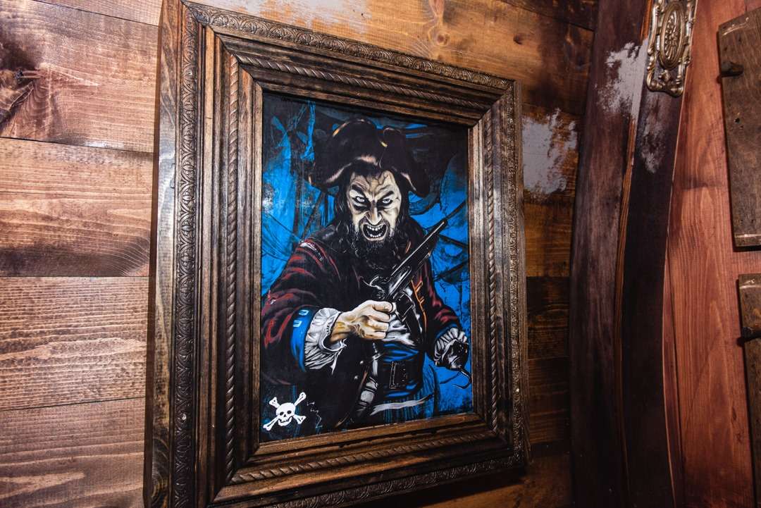 Framed painting of an angry pirate holding a pistol, with a dark blue background and wood-paneled wall.