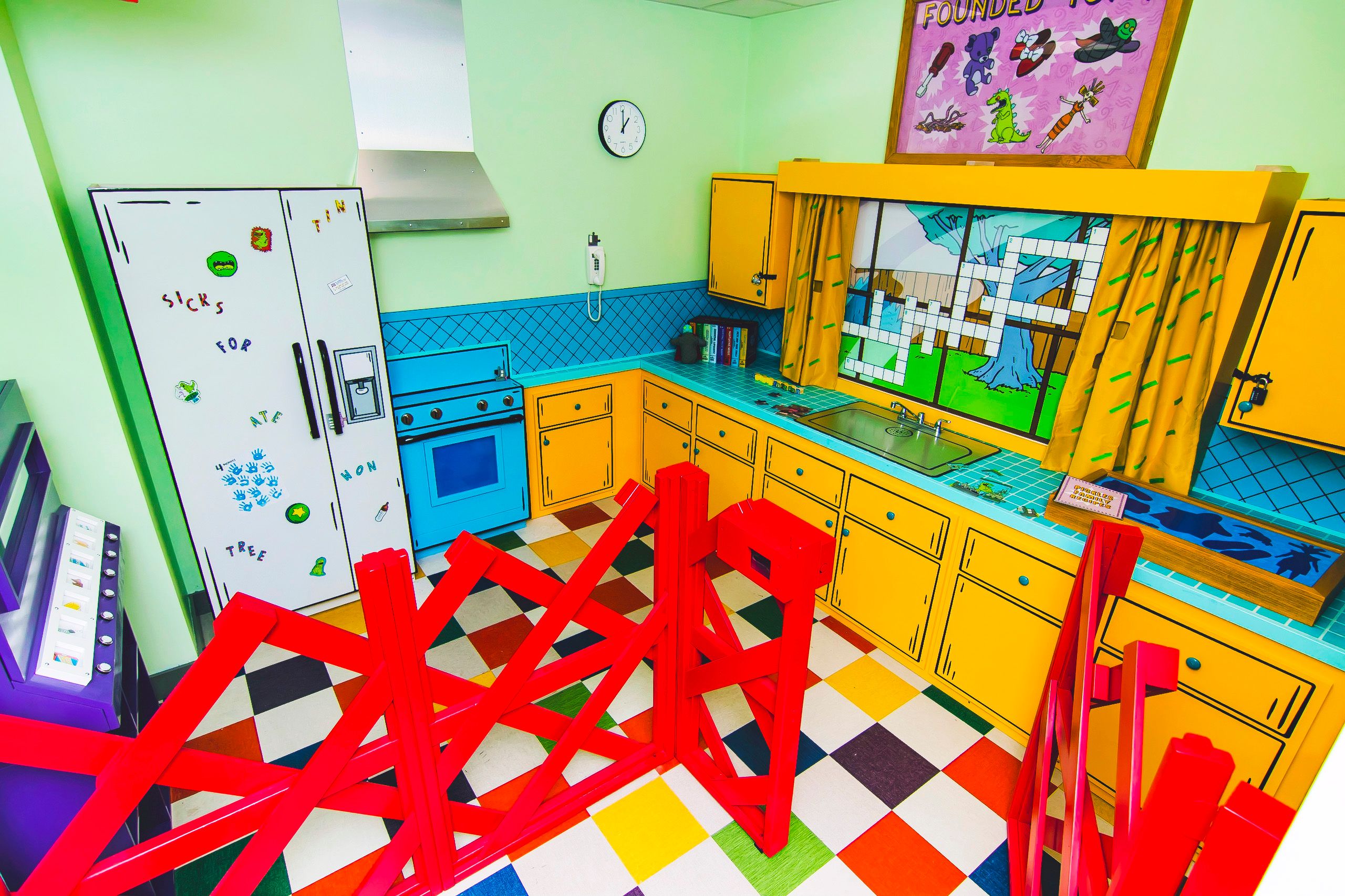 Colorful kitchen with yellow cabinets, a blue stove, and a patterned floor. Bright red barricades block access.