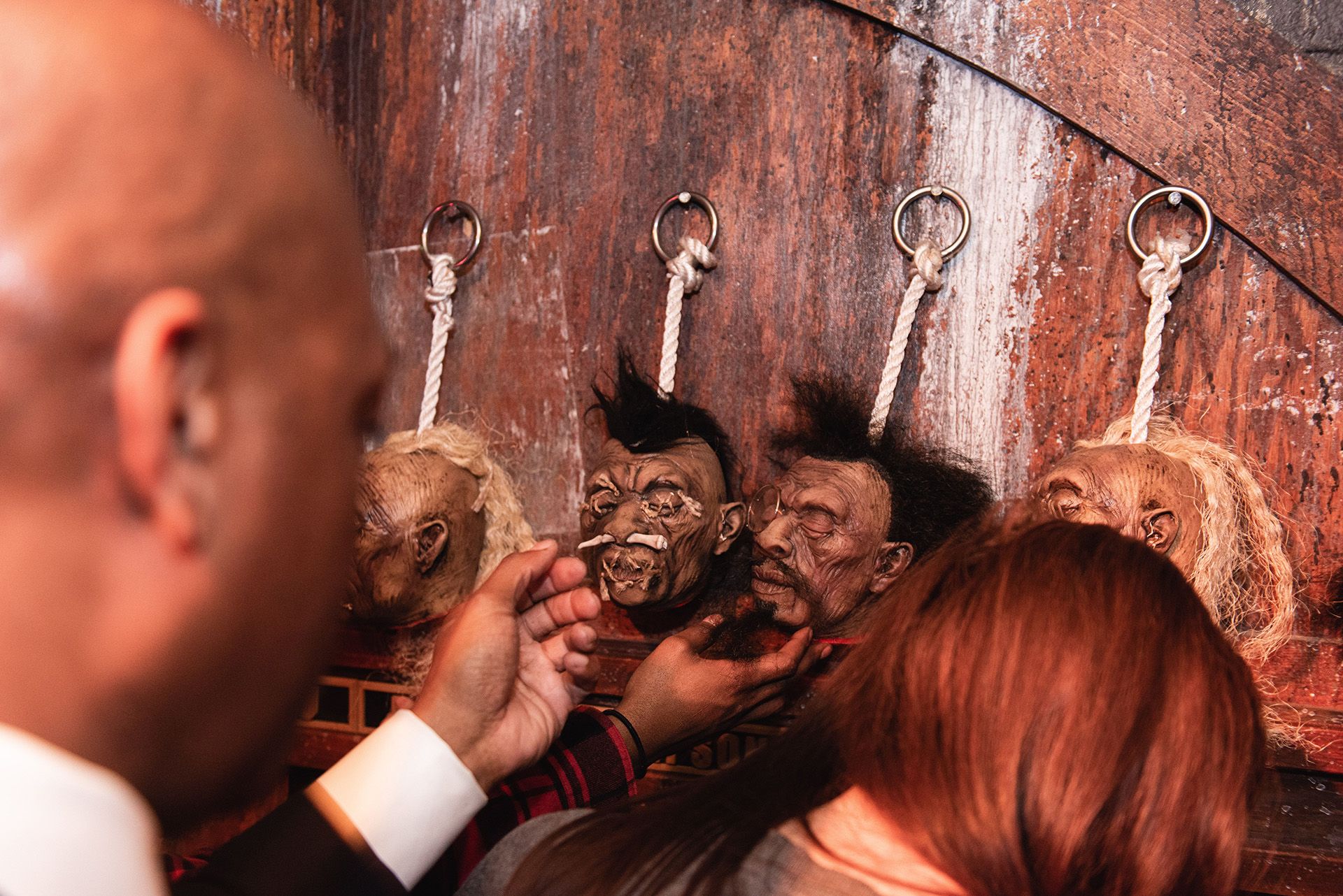 Close-up of a person examining mounted, lifelike heads on a wall, with another person's hand visible in the foreground.