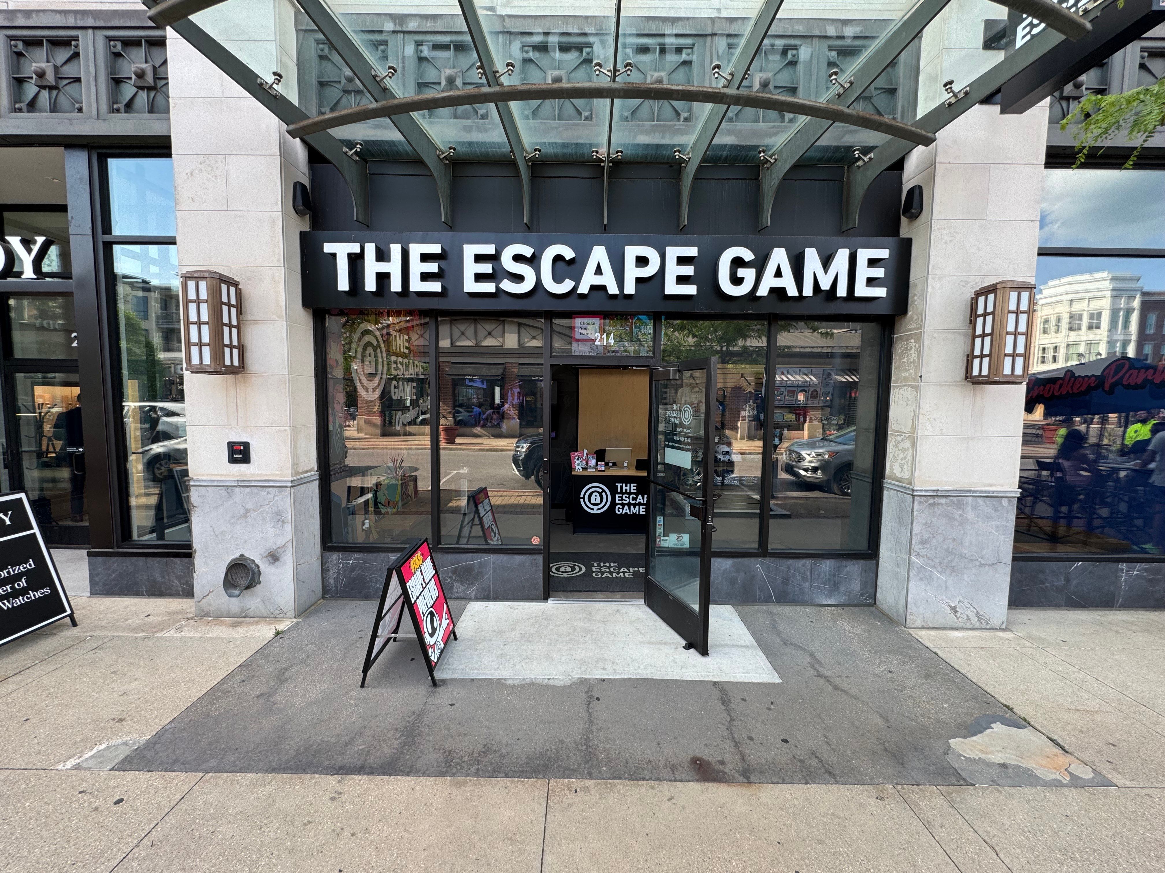 Exterior view of "The Escape Game" entrance featuring large signage, glass doors, and a pedestrian walkway.
