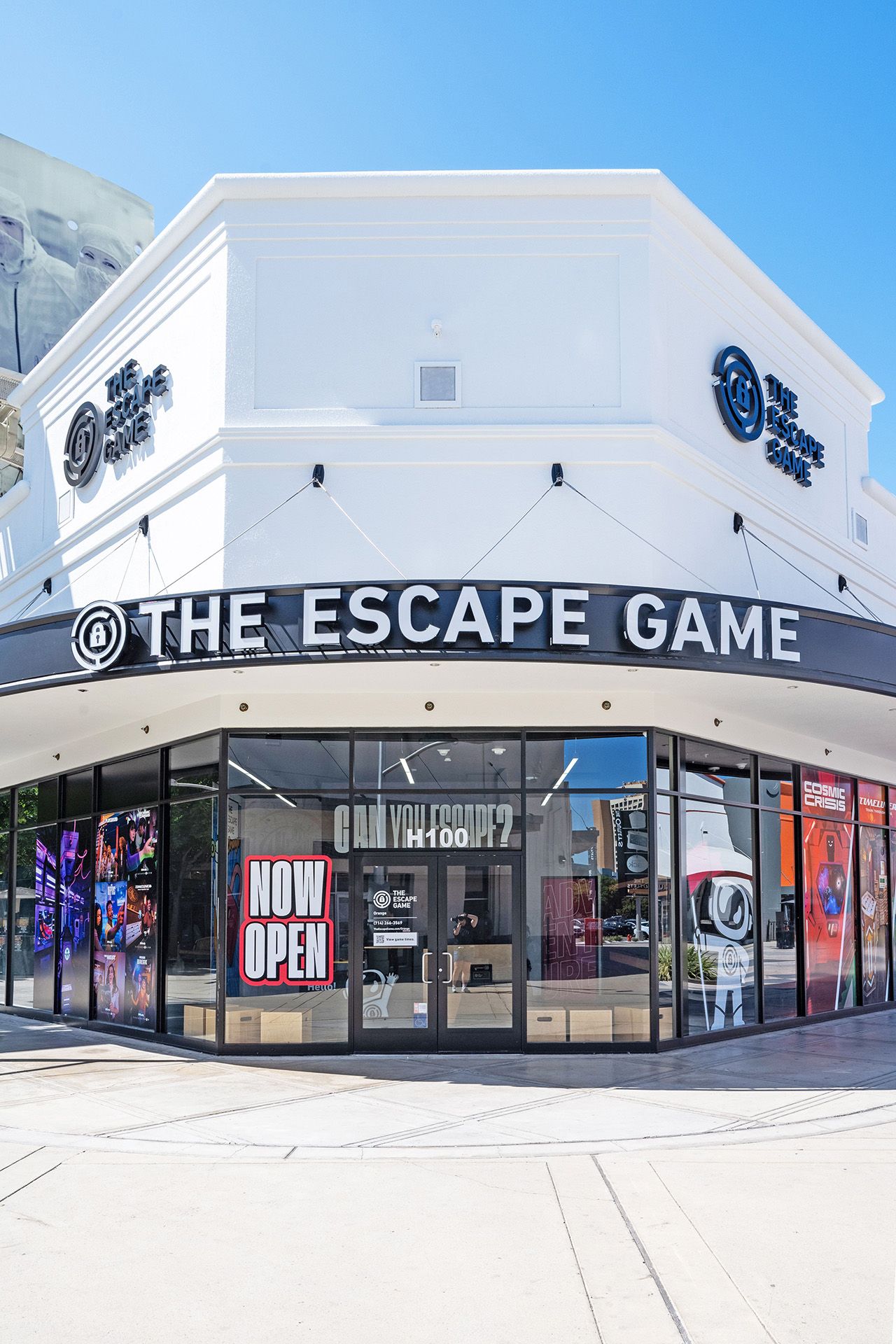 Exterior of "The Escape Game" with large windows, featuring a "NOW OPEN" sign and colorful promotional posters.