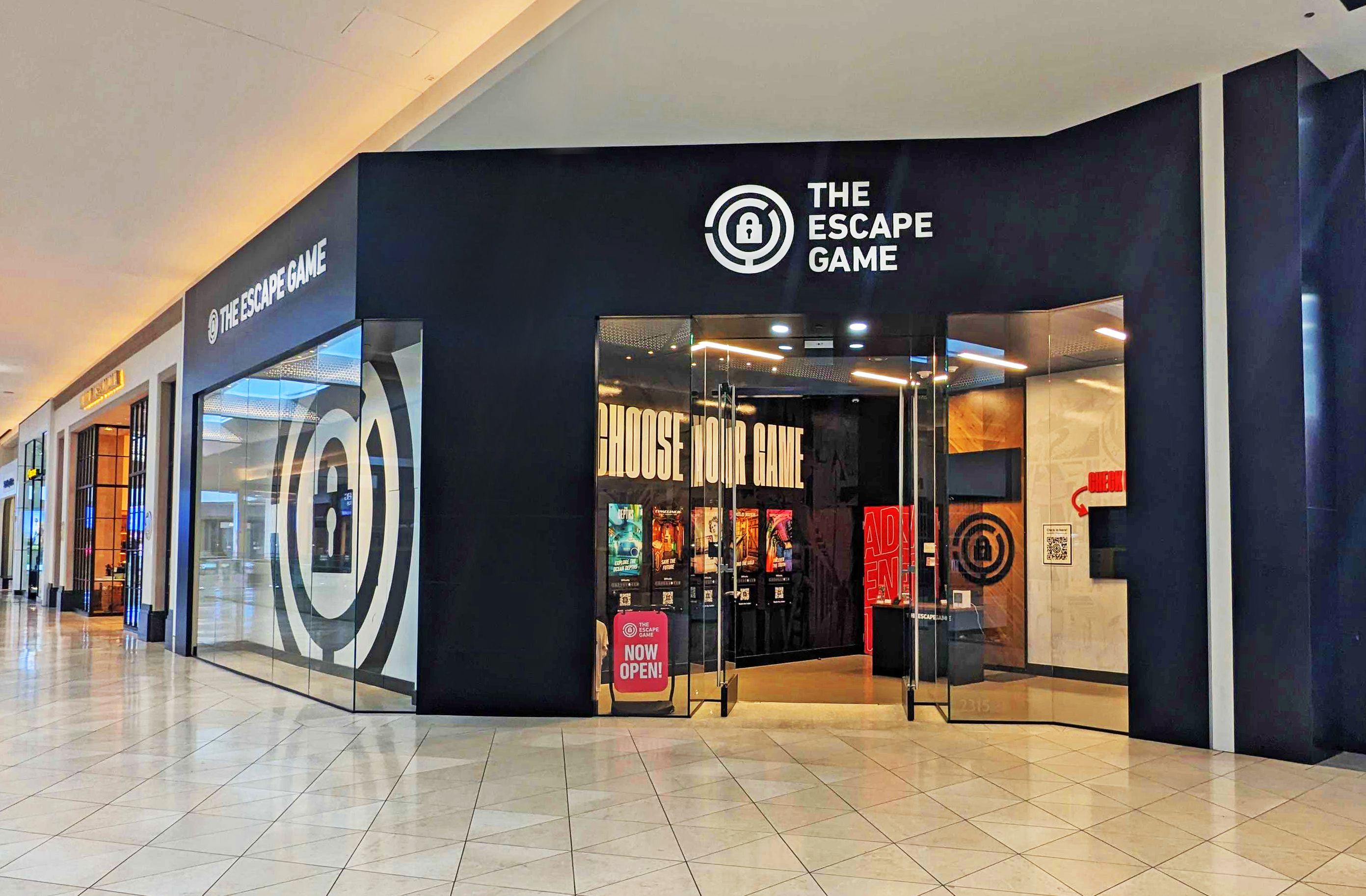 Entrance of "The Escape Game" with large windows and a prominent sign. Displays include "Choose Your Game" and "Now Open."