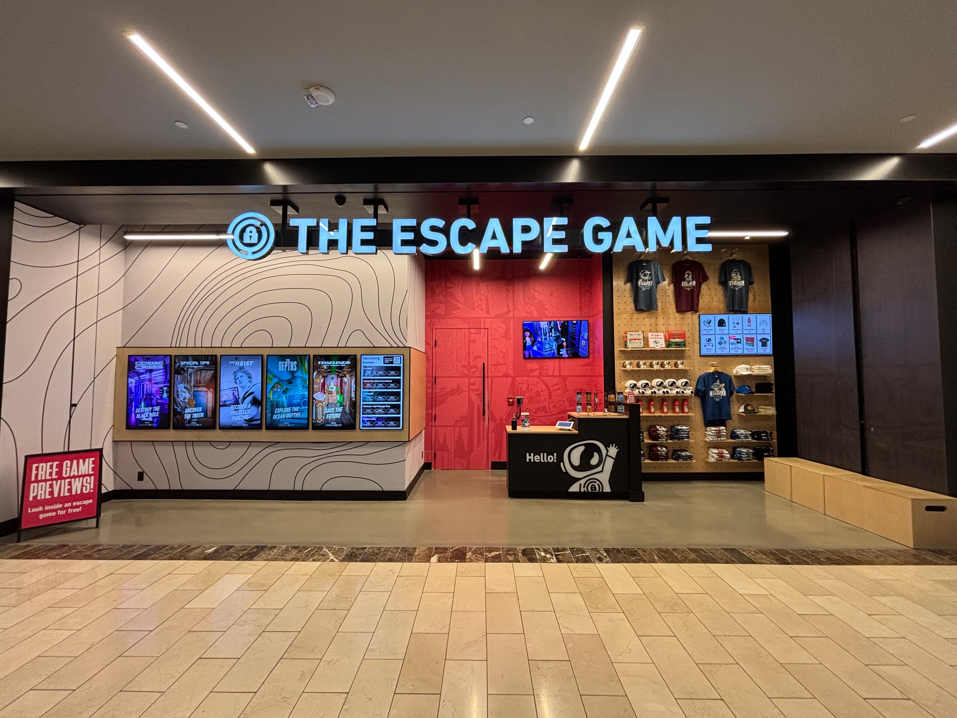 Entrance of "The Escape Game" featuring a bright sign, game previews on screens, and merchandise displayed on the wall.