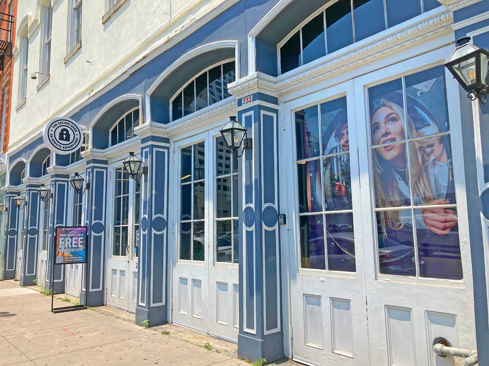 Exterior of a building with blue accents, featuring large windows, a sign for an escape room, and colorful promotional banners.
