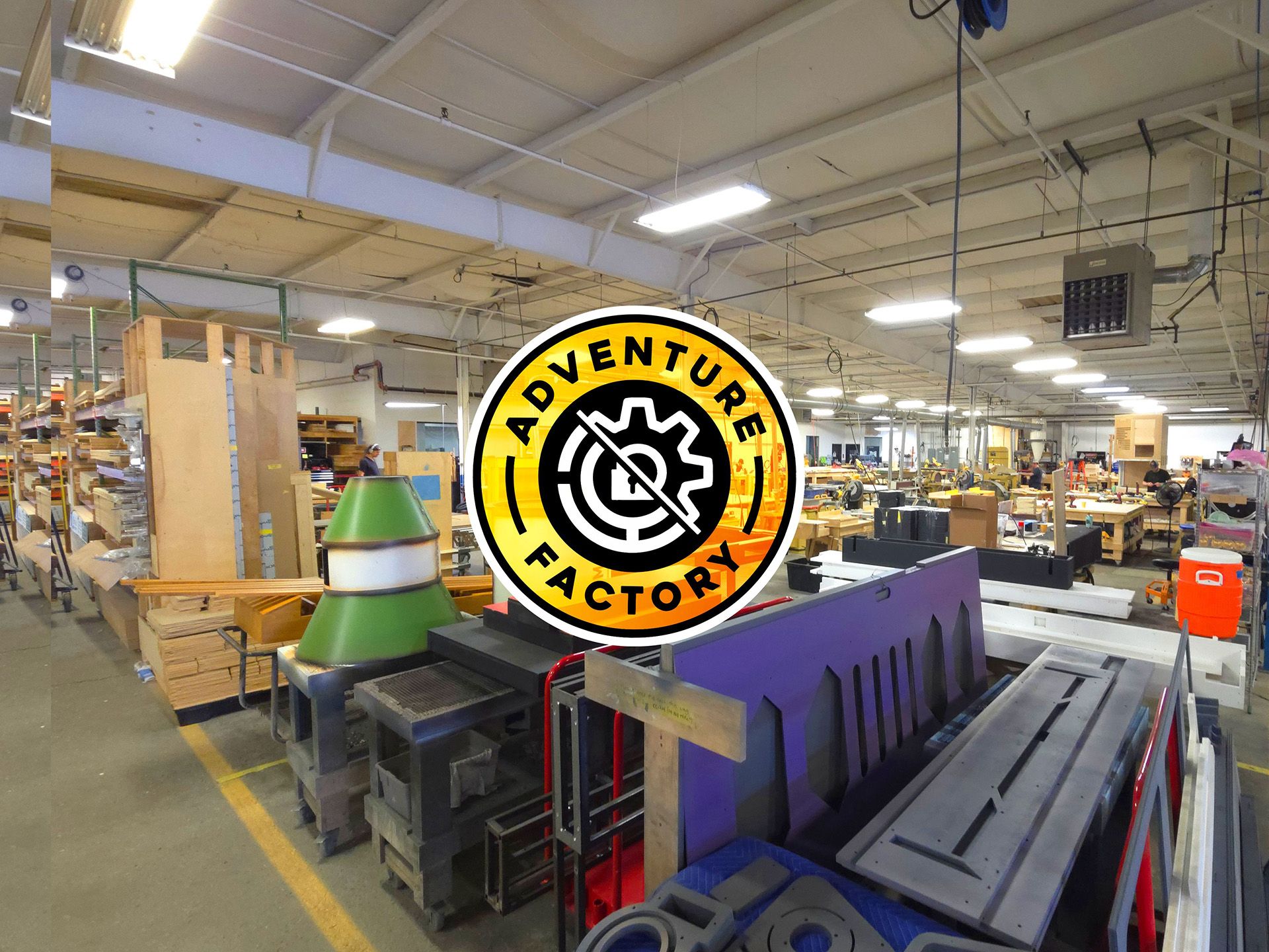 A spacious workshop filled with tools, materials, and workstations. The logo "Adventure Factory" is prominently displayed in the center.