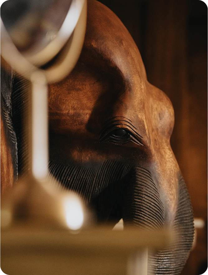 Close-up of a wooden elephant sculpture partially obscured by a blurred decorative object in the foreground.