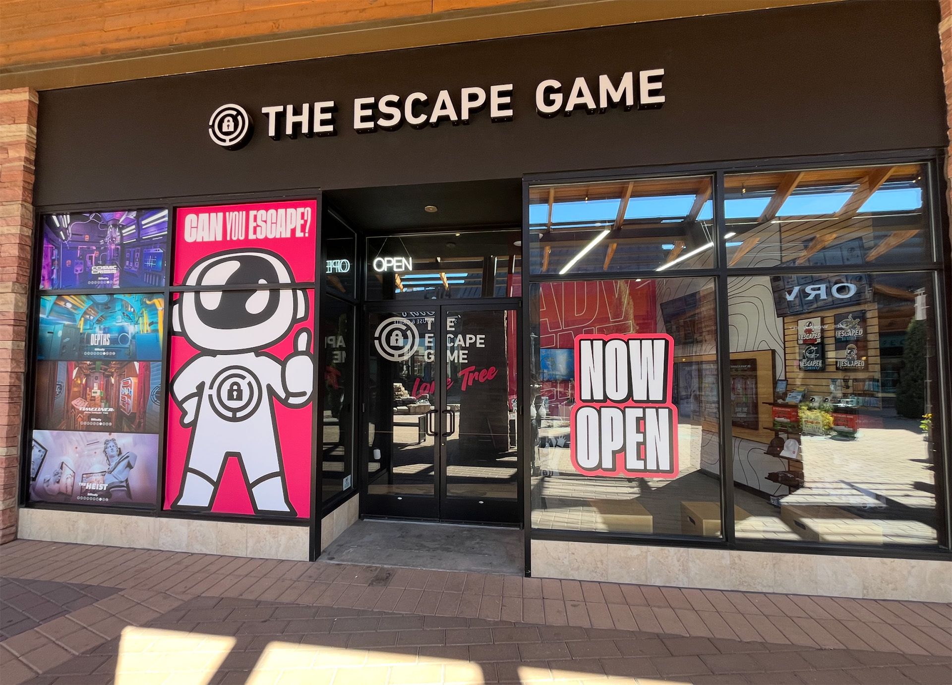 Exterior of "The Escape Game" featuring a large pink graphic, "CAN YOU ESCAPE?" and "NOW OPEN" sign.